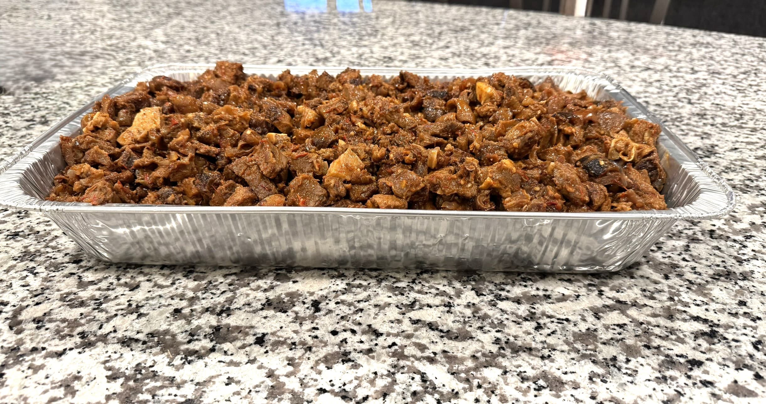 Friends laughing and sharing a tray of spicy meat at an outdoor party.